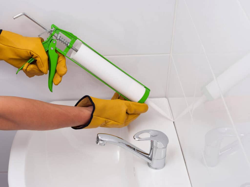 expert applying caulking around a bathroom sink